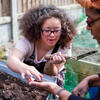 young Black woman holding a trowel works at raised garden bed with female elder
