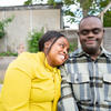 Black woman and adult disabled son sit close together outdoors, smiling