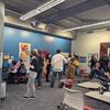 people sitting or standing in small groups, viewing or discussing the exhibit of a variety of works on the walls in the background